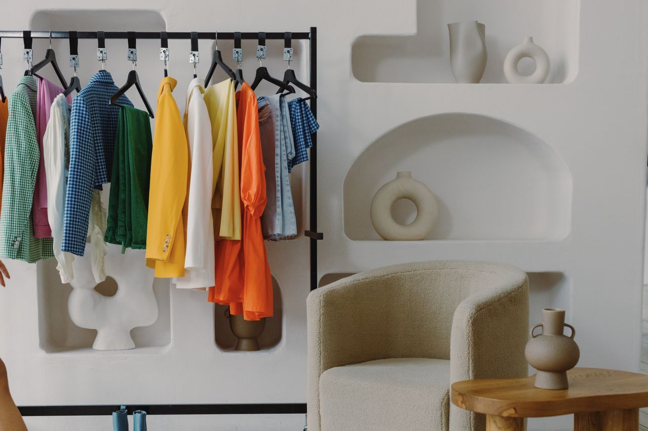 Boucle chair beside a colorful clothing rack and sculptural shelves