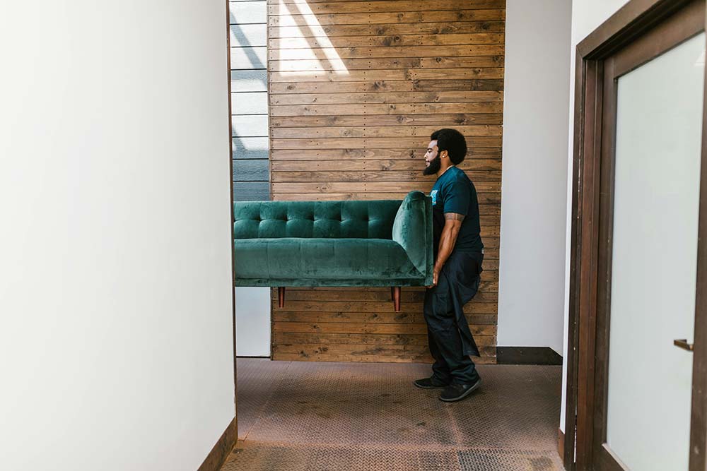Mover carrying a green velvet sofa through a hallway during interior installation