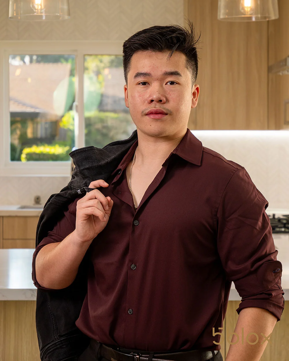 Kelvin Nguyen standing in a kitchen holding a coat over his shoulder